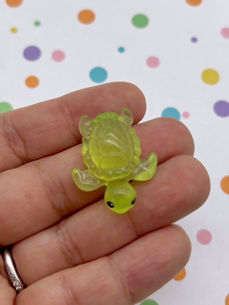 A hand holding a small, green turtle-shaped object against a background with colorful polka dots.