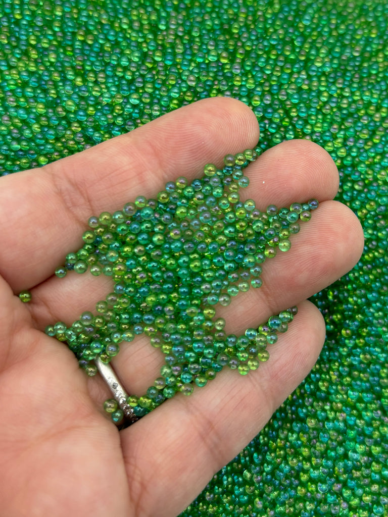 a hand is holding some beads on a green cloth