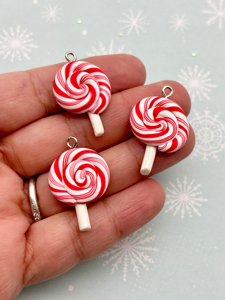 A hand holding three red and white striped lollipops against a snowy background.