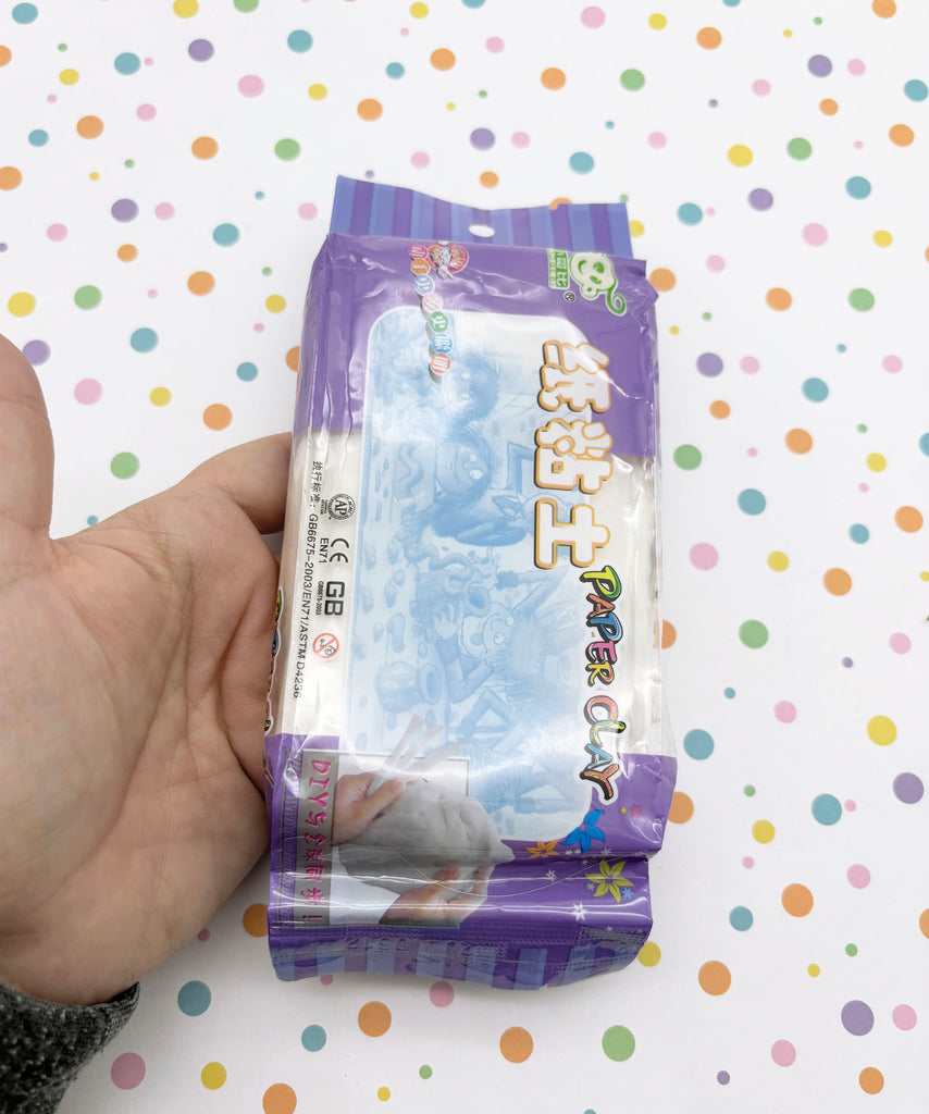 A hand is holding a package of Play Clay, which is a type of clay product.