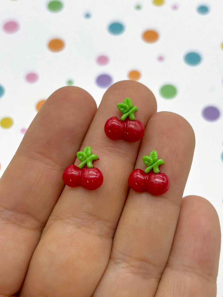 a pair of tiny red cherries on a person's finger