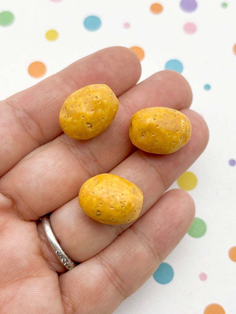 A hand holding three small, round yellow objects against a background with colorful polka dots.