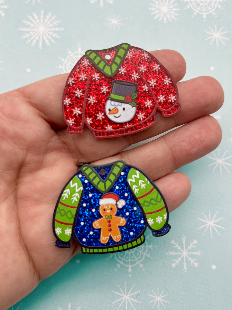 A hand holding two Christmas-themed brooches, one with a snowman and the other with a gingerbread man.