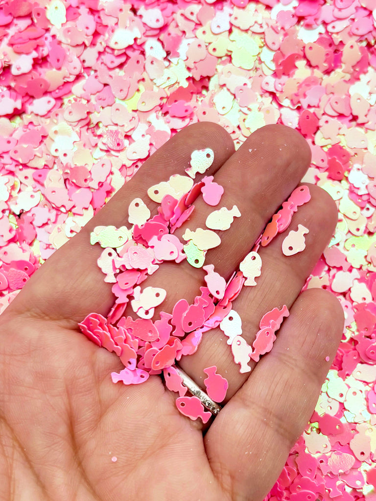 A hand holding a pile of pink and white sequin-like objects, creating a visually appealing and colorful display.