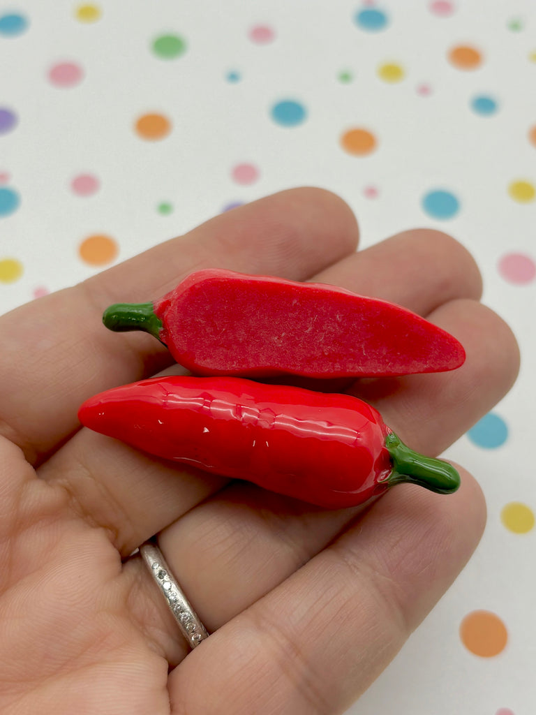 a hand holding two tiny red peppers