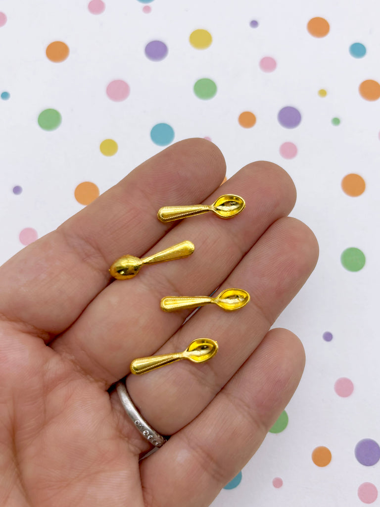 A hand holding four small gold-colored spoons against a background with colorful polka dots.