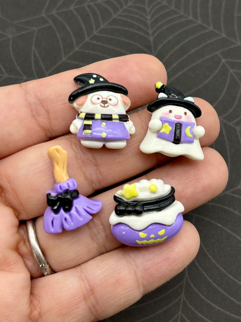 A hand holding four small, colorful plastic figurines representing a witch, ghost, broomstick, and a pumpkin.