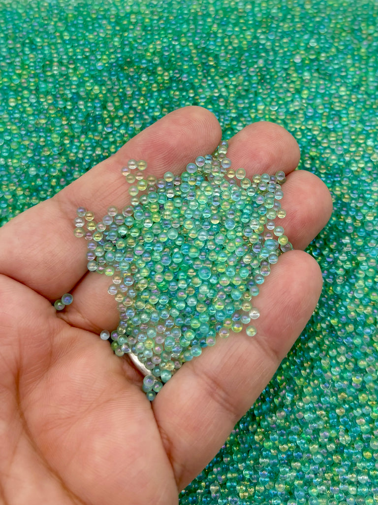 A hand holding a pile of multicolored beads against a background of green and blue beads.