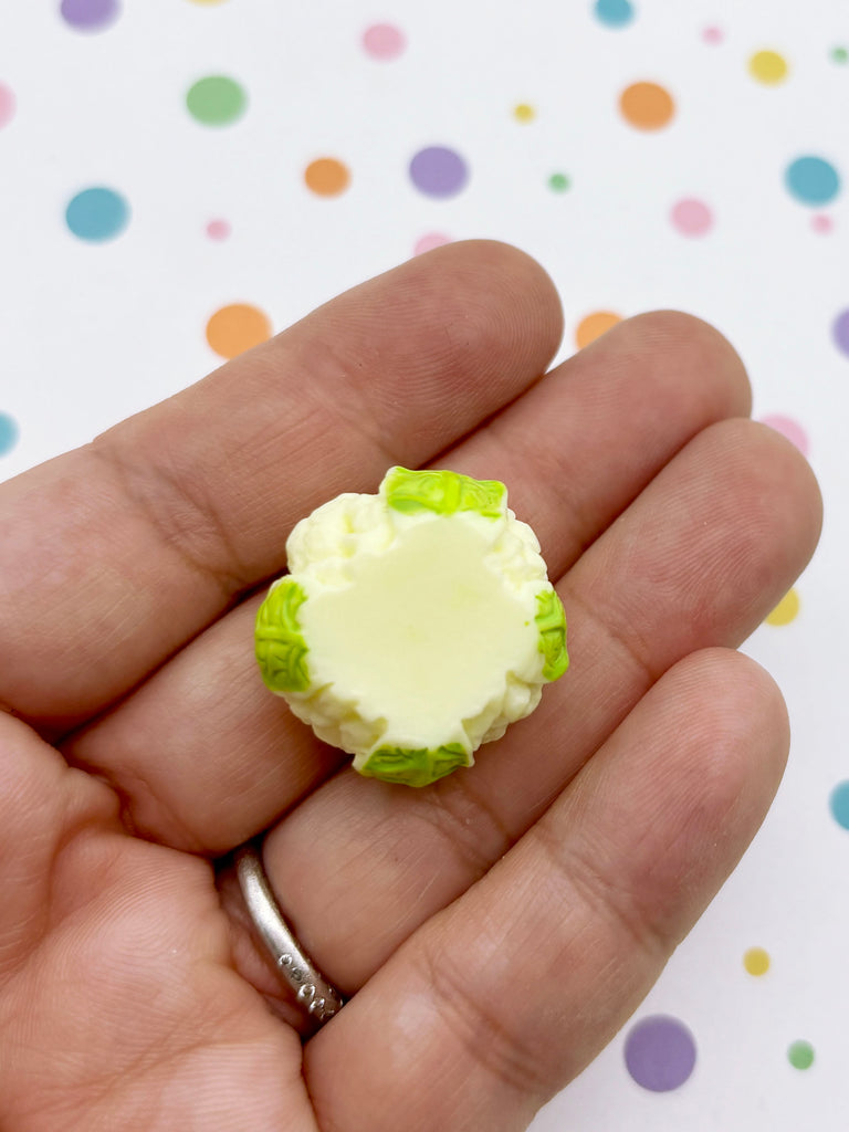 A hand holding a small, round object with green and white colors against a background with colorful polka dots.