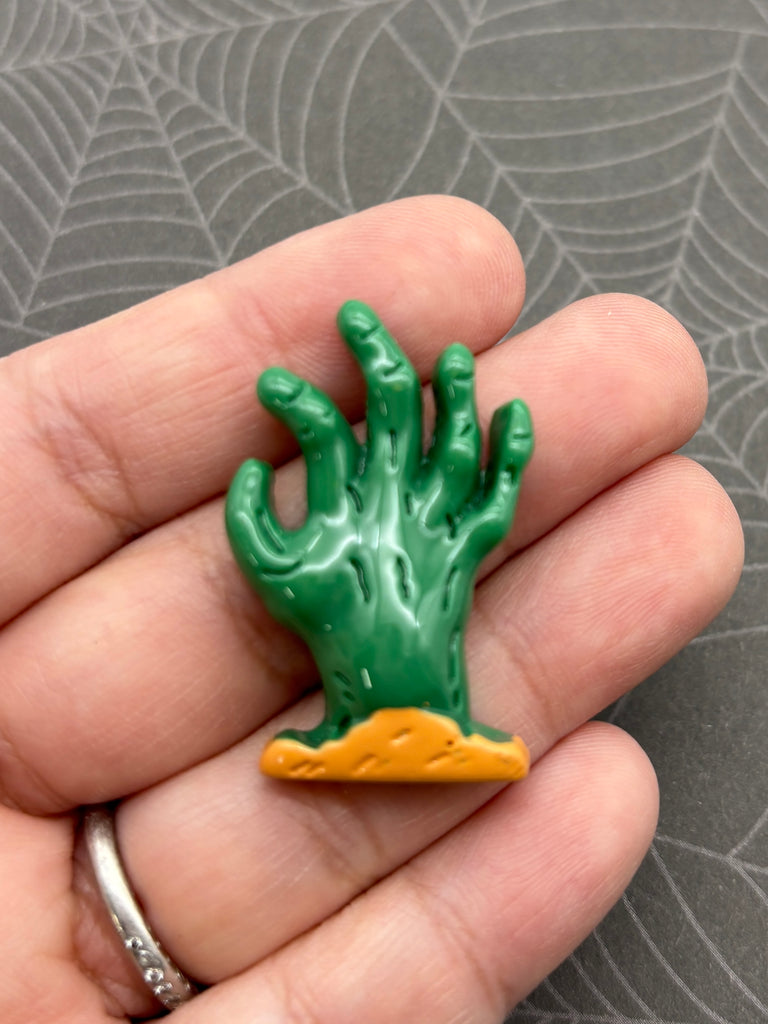 A hand holding a green cactus-shaped object with a yellow base, against a spider web background.