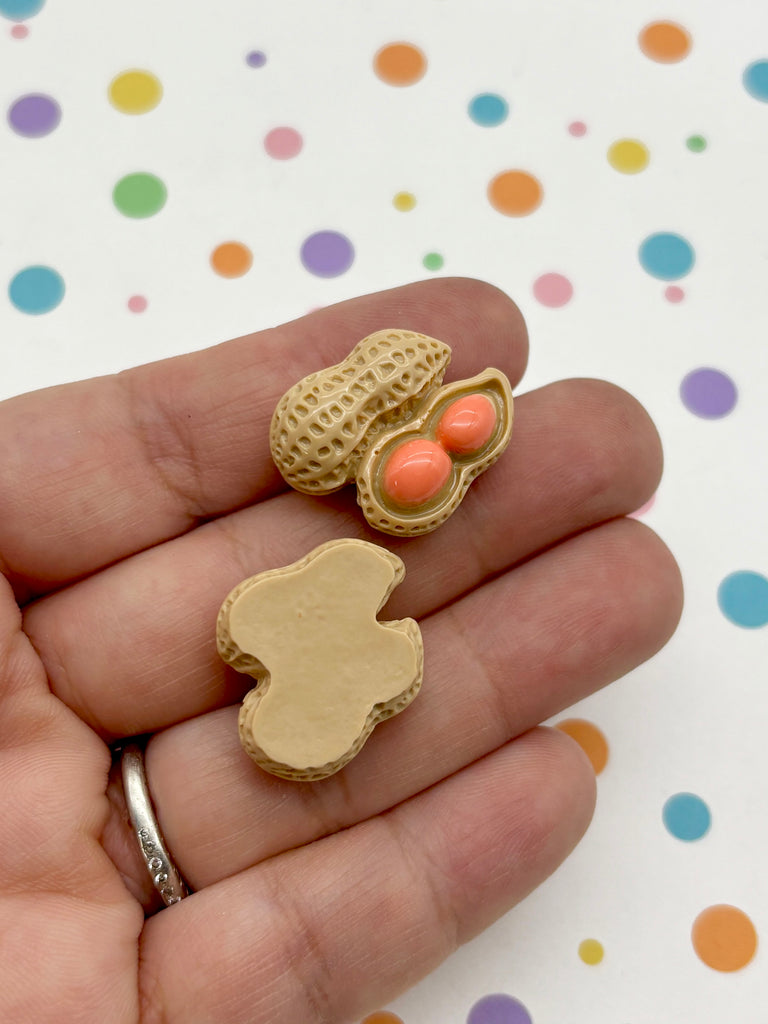 A hand holding a peanut shell with two orange candies inside, against a background of colorful polka dots.