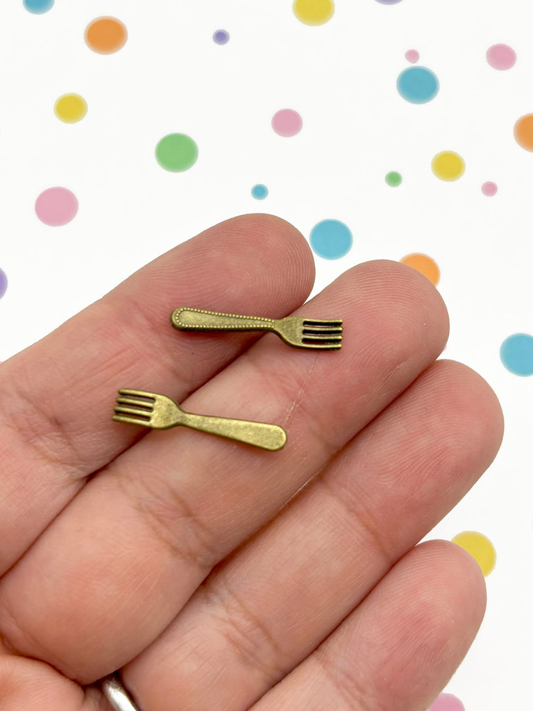 A hand holding two small gold-colored forks against a background with colorful polka dots.