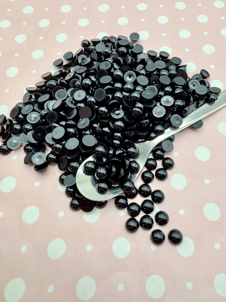 A pile of black beads is scattered on a pink and white polka dot background, with a spoon lying nearby.