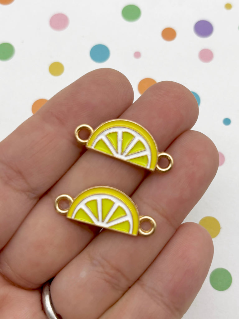 A hand holding two yellow enamel charms shaped like lemon slices.