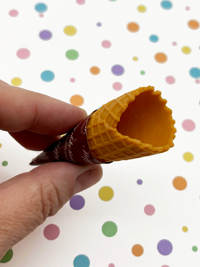 A hand is holding a partially eaten waffle cone against a background of colorful polka dots.