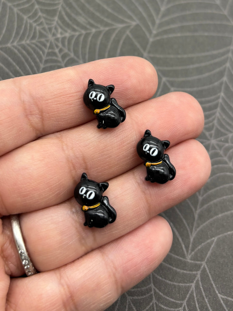 A hand holding three small black cat-shaped charms with white eyes.