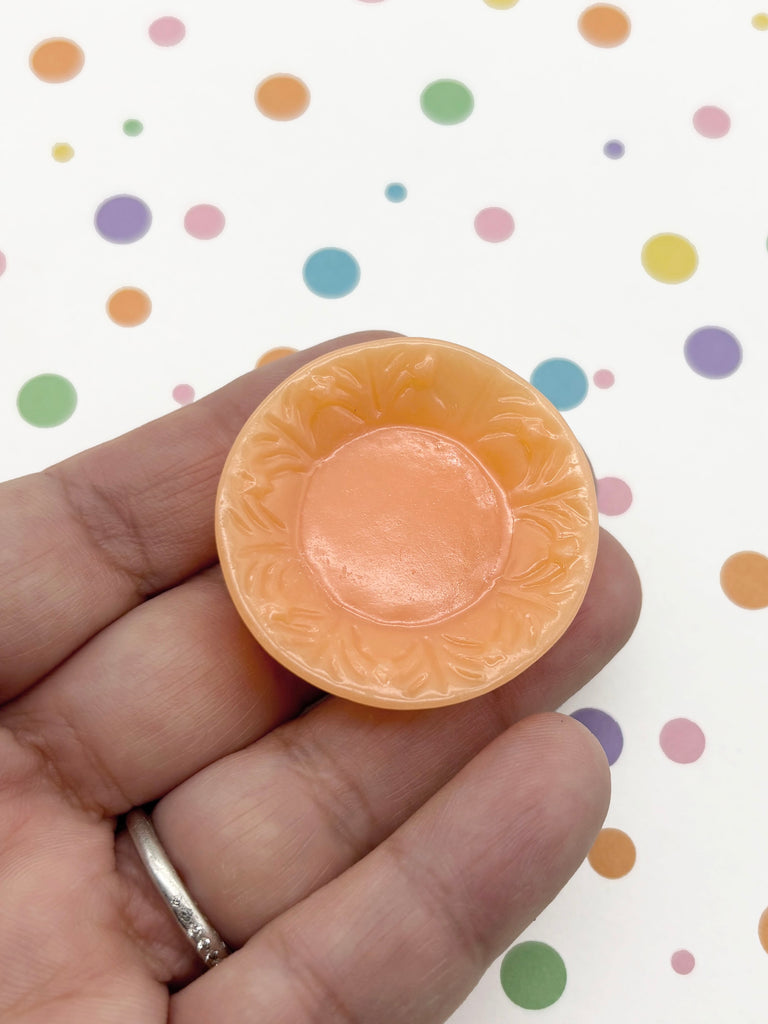 A hand holding a small orange-colored object with a floral design, against a background with colorful polka dots.