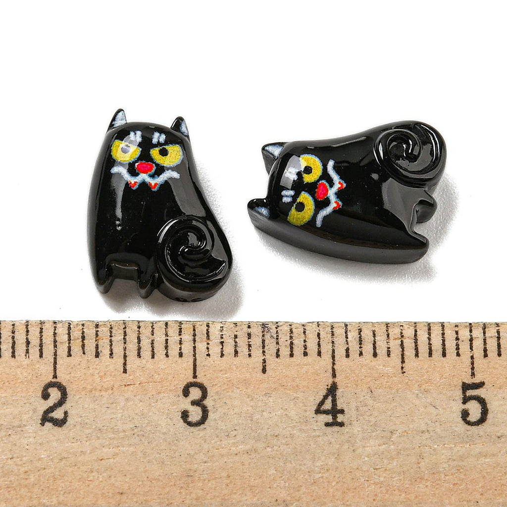 two black cat shaped buttons sitting next to a ruler