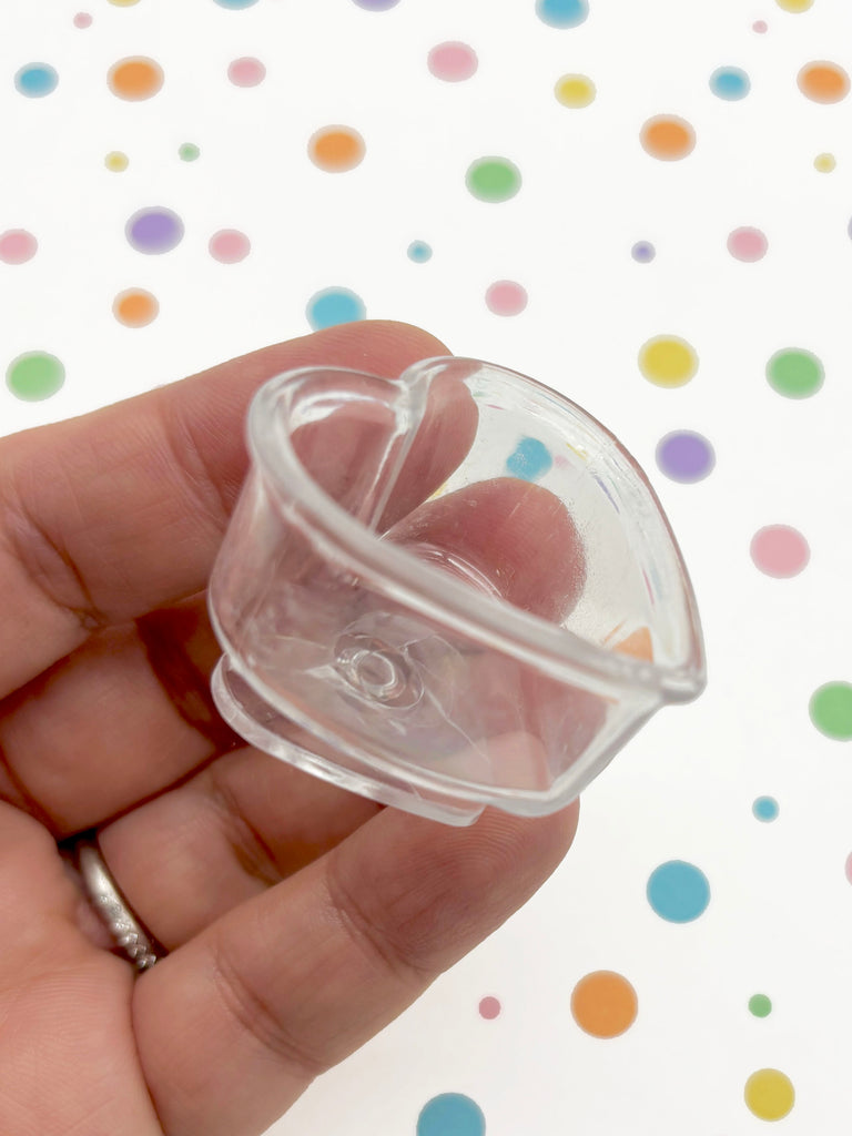 A hand is holding a clear plastic cup with a heart-shaped opening, against a background of colorful polka dots.