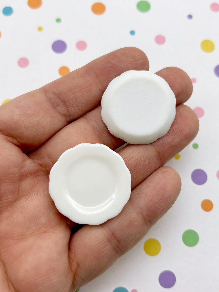A hand holding two white, round, ceramic plates against a background with colorful polka dots.