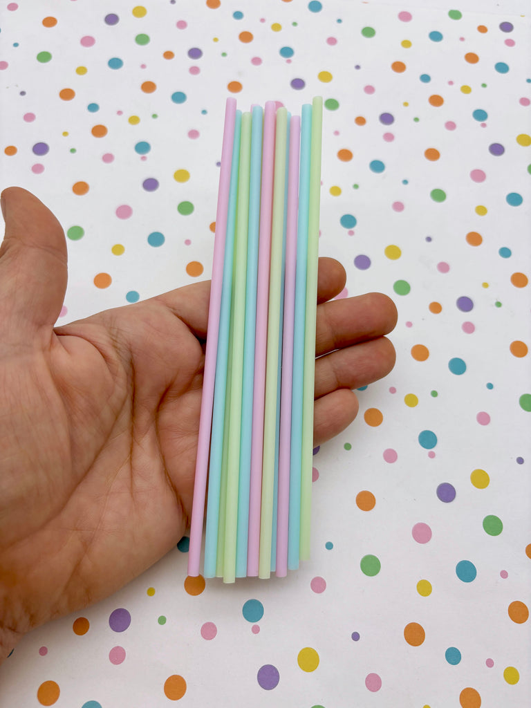 A hand holding a bunch of colorful straws against a background with polka dots.