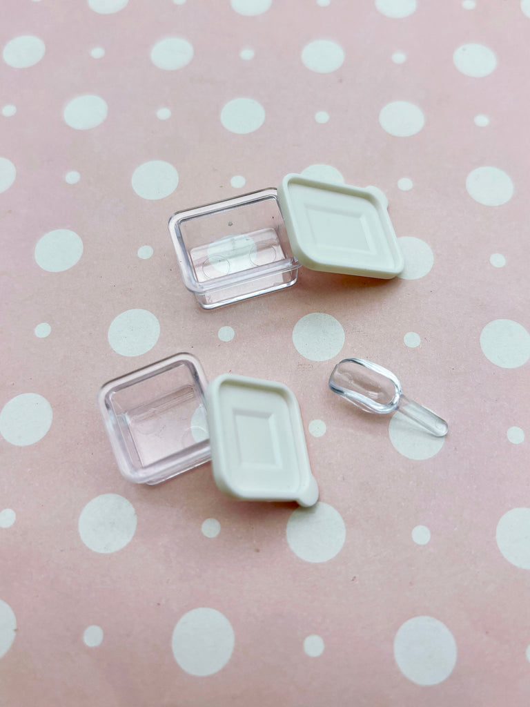 a pink polka dot background with two clear plastic containers and a small plastic scoop.