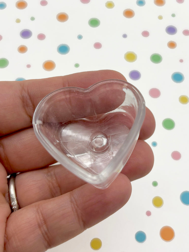 A hand is holding a clear heart-shaped object against a background with colorful polka dots.