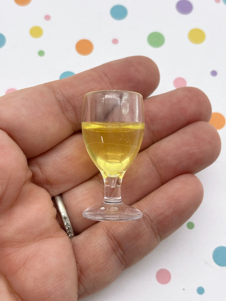 A hand holding a small glass of yellow liquid against a background with colorful polka dots.