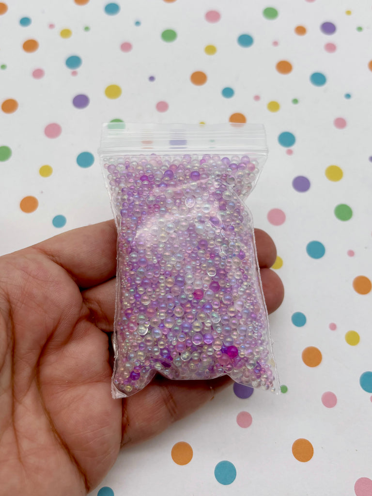 A hand is holding a small bag filled with colorful beads against a background of colorful polka dots.