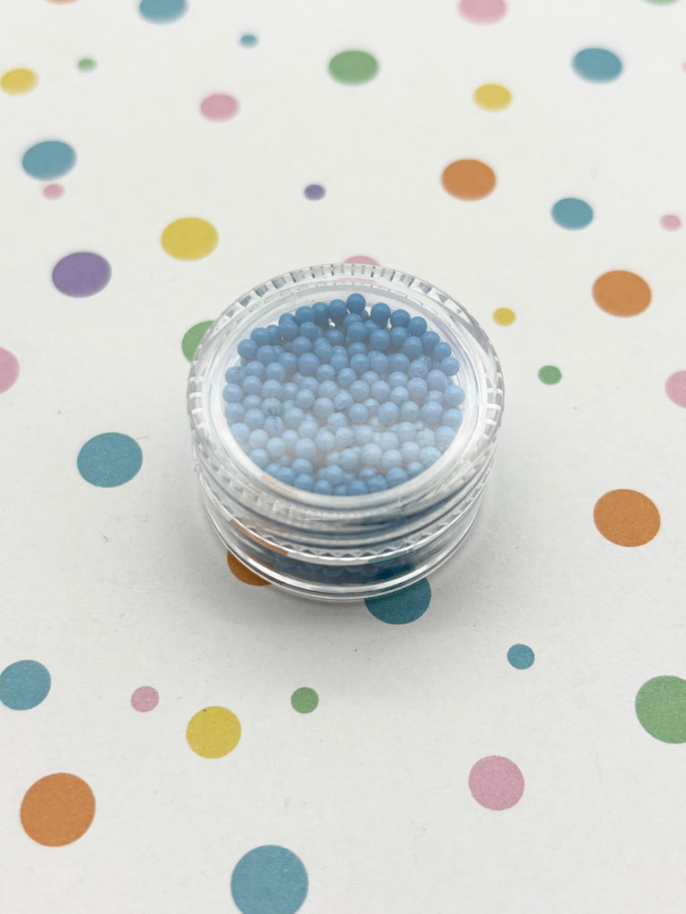 A clear container filled with blue beads is placed on a white surface with colorful polka dots.