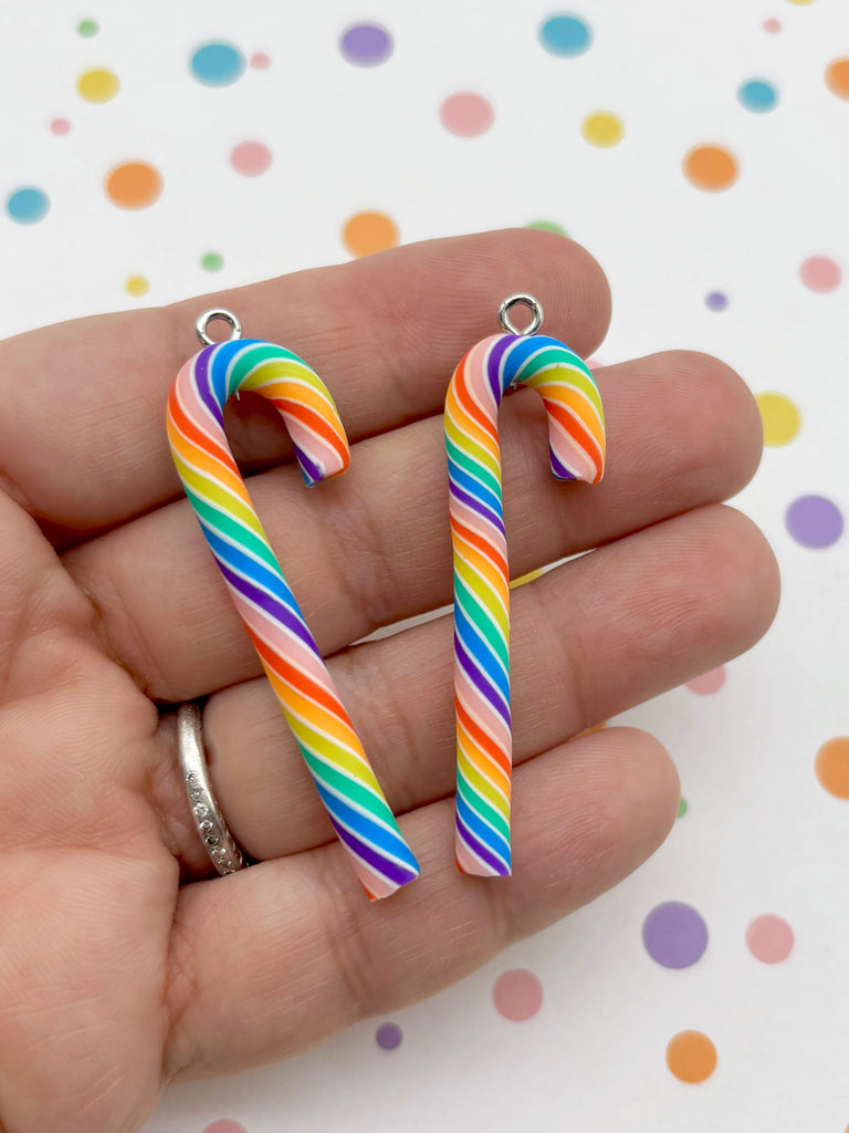 A hand holding two colorful candy cane-shaped charms against a background with polka dots.