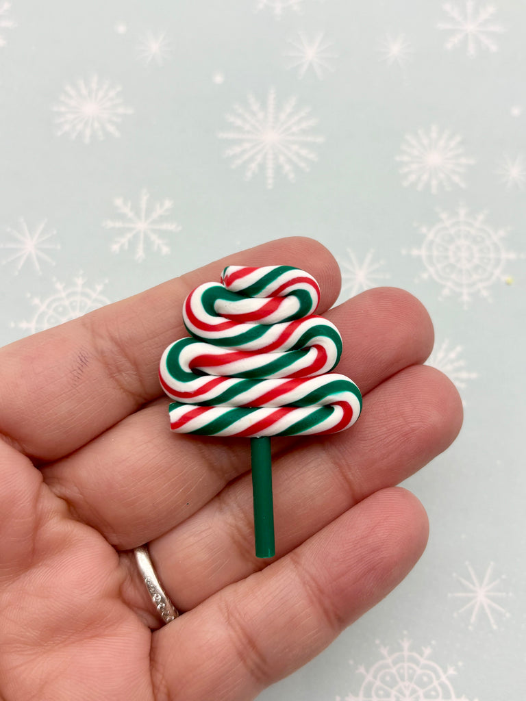 A hand holding a small candy cane tree-shaped object against a background of snowflakes.