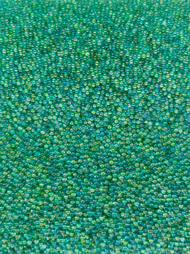 The image is a close-up of a textured surface covered in numerous small, round, green and blue beads or stones, creating a visually striking and intricate pattern.