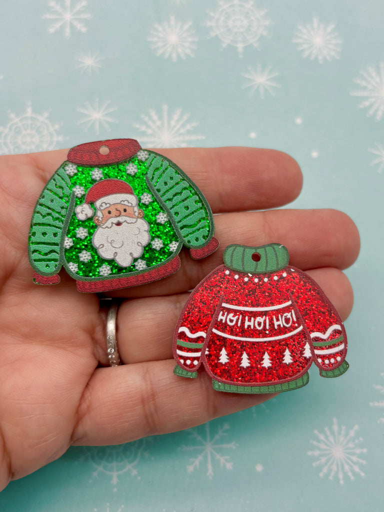 A hand holding two Christmas-themed ornaments against a snowy background.