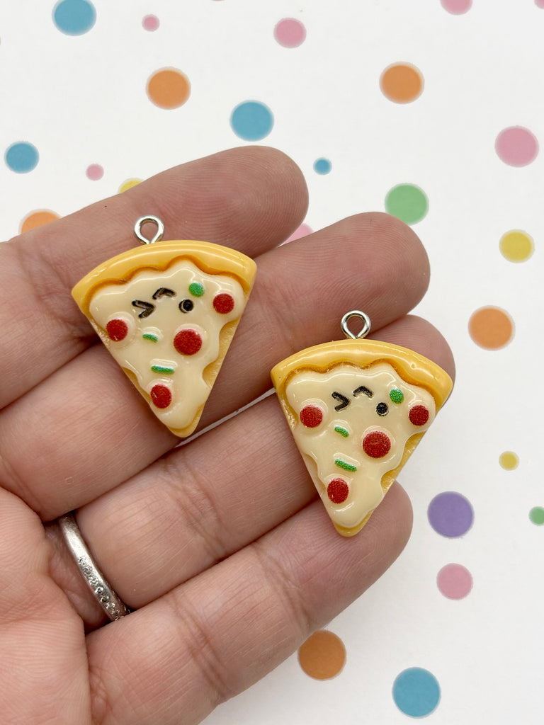 A hand holding two small, colorful charms shaped like slices of pizza.