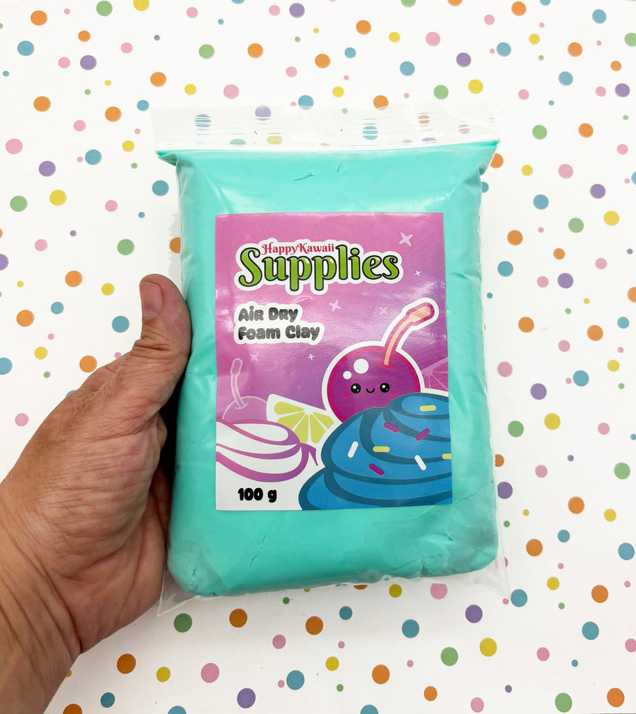 A hand is holding a package of HappyKawaii Supplies' Air Day Foam Clay, which is a light blue-green color. The package has a label with a cartoon image of a cherry and a cupcake, along with the text "HappyKawaii Supplies" and "Air Day Foam Clay".