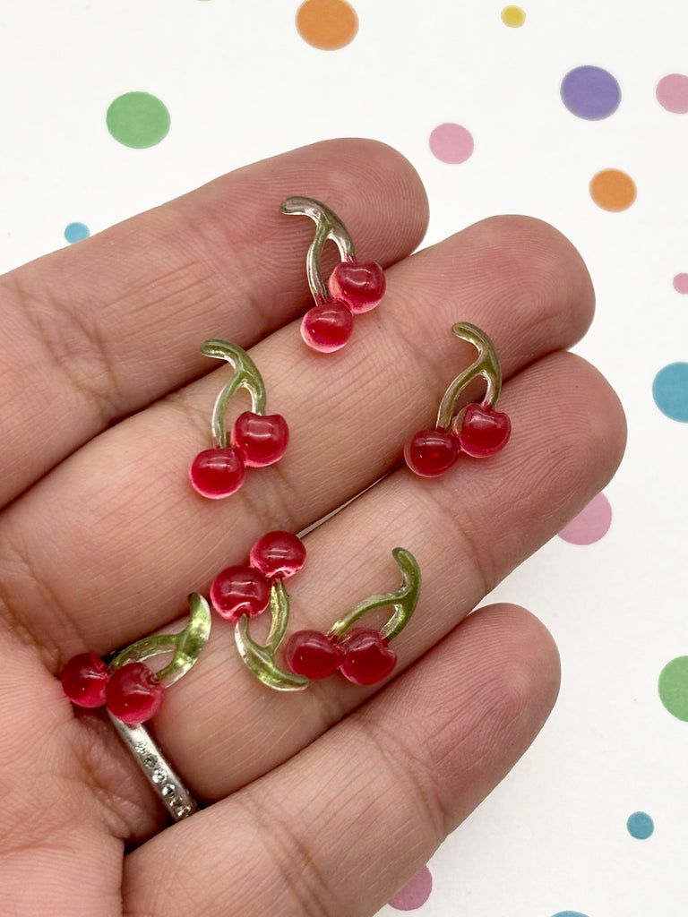 A hand holding several small red and green cherries against a background with colorful polka dots.