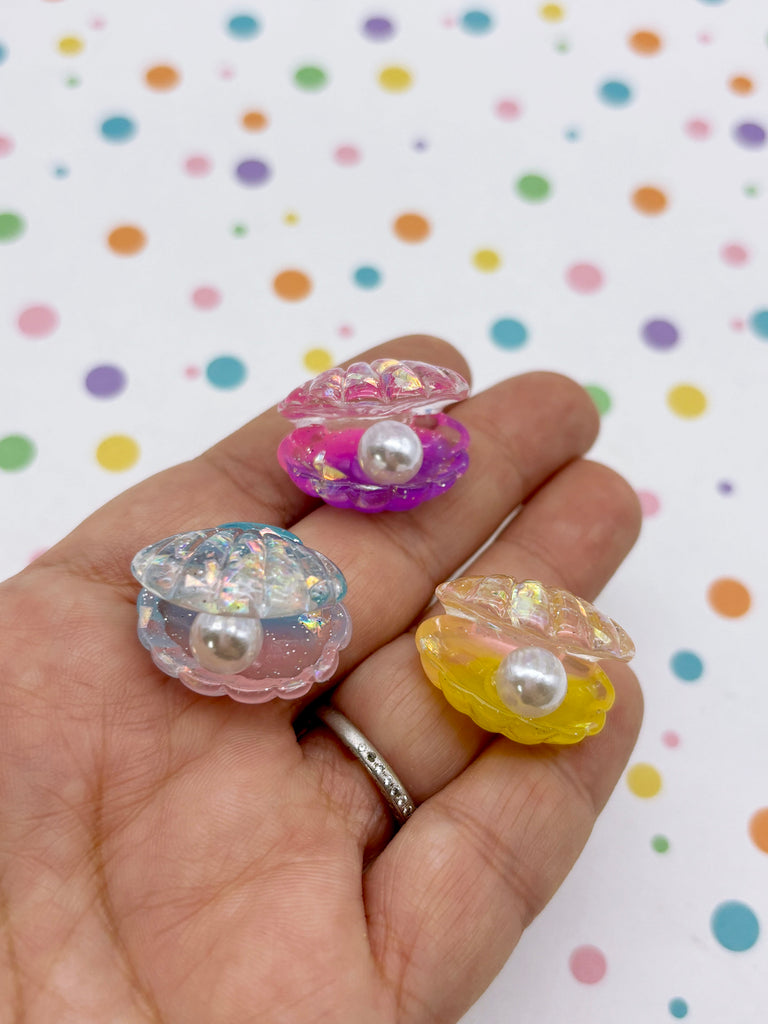A hand holding three colorful seashell-shaped objects against a background with polka dots.