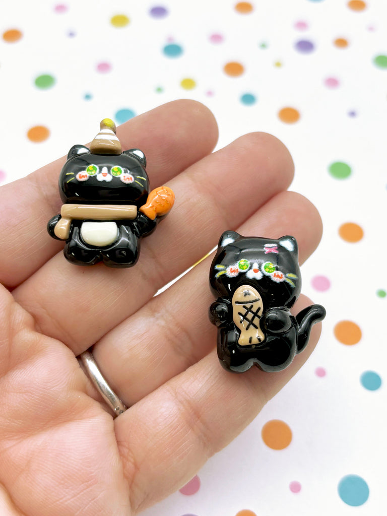 a hand holding two small black cat figurines