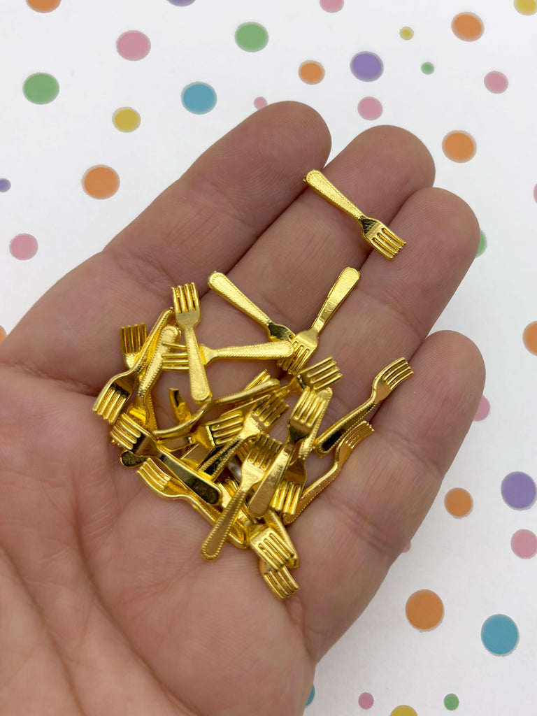 A hand holding a pile of small, gold-colored plastic forks and spoons against a background with colorful polka dots.