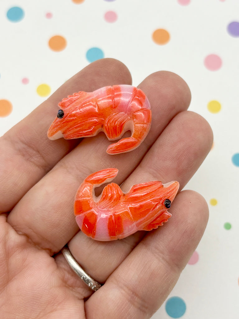 A hand holding two small, orange and pink shrimp-shaped objects against a background with colorful polka dots.