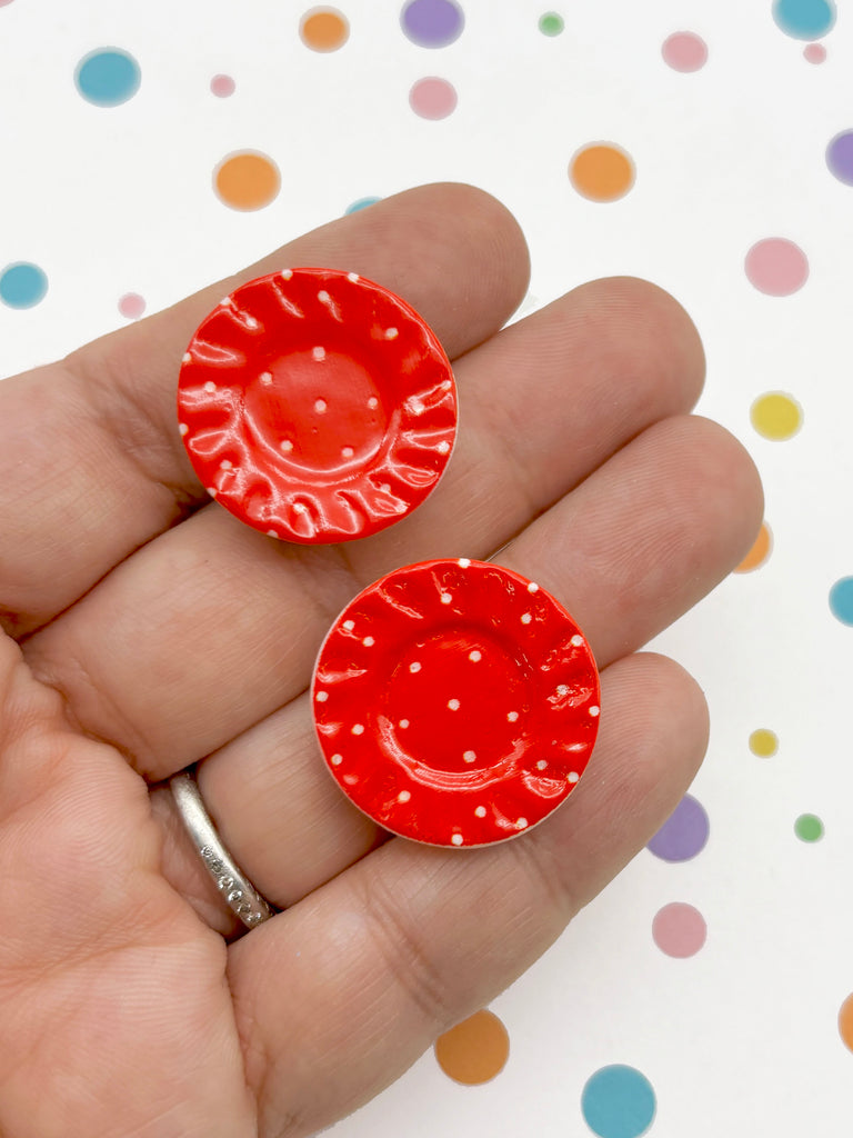 A hand holding two red, polka-dotted ceramic plates against a background with colorful polka dots.