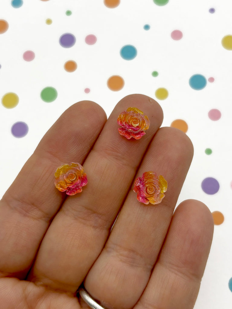 a person holding a pair of pink and yellow flowers on their fingers