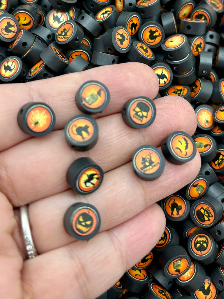A hand holding a collection of small black beads with Halloween-themed designs, including bats, skulls, and bats.