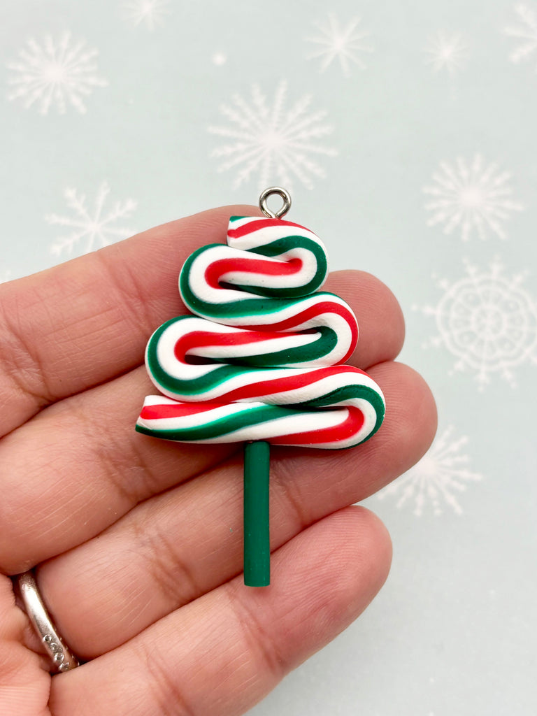 A hand holding a Christmas tree-shaped pendant made of candy canes in red, white, and green colors.