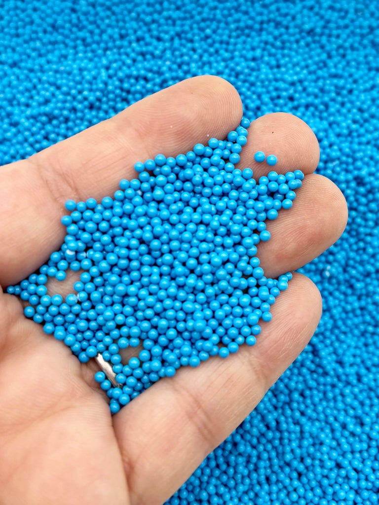 A hand holding a pile of small, round blue beads against a blue background.