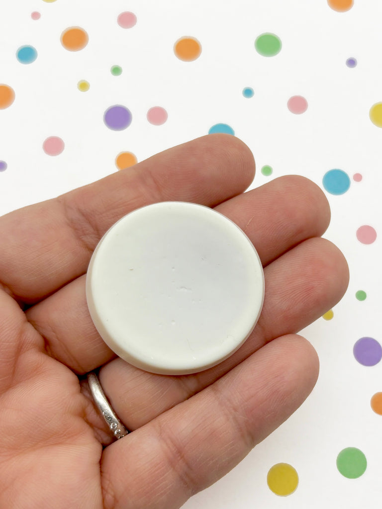 A hand holding a white, round object against a background of colorful polka dots.