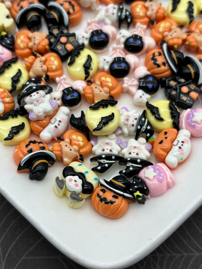 A collection of Halloween-themed small plastic figurines, including bats, pumpkins, and other spooky or festive elements, arranged on a white surface.