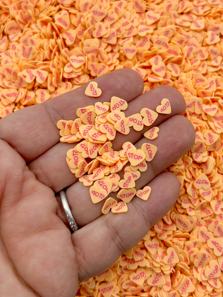 A hand holding a pile of small orange heart-shaped objects with the word "STOP" printed on them.
