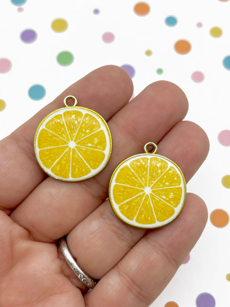 A hand holding two round charms shaped like lemon slices against a background with colorful polka dots.